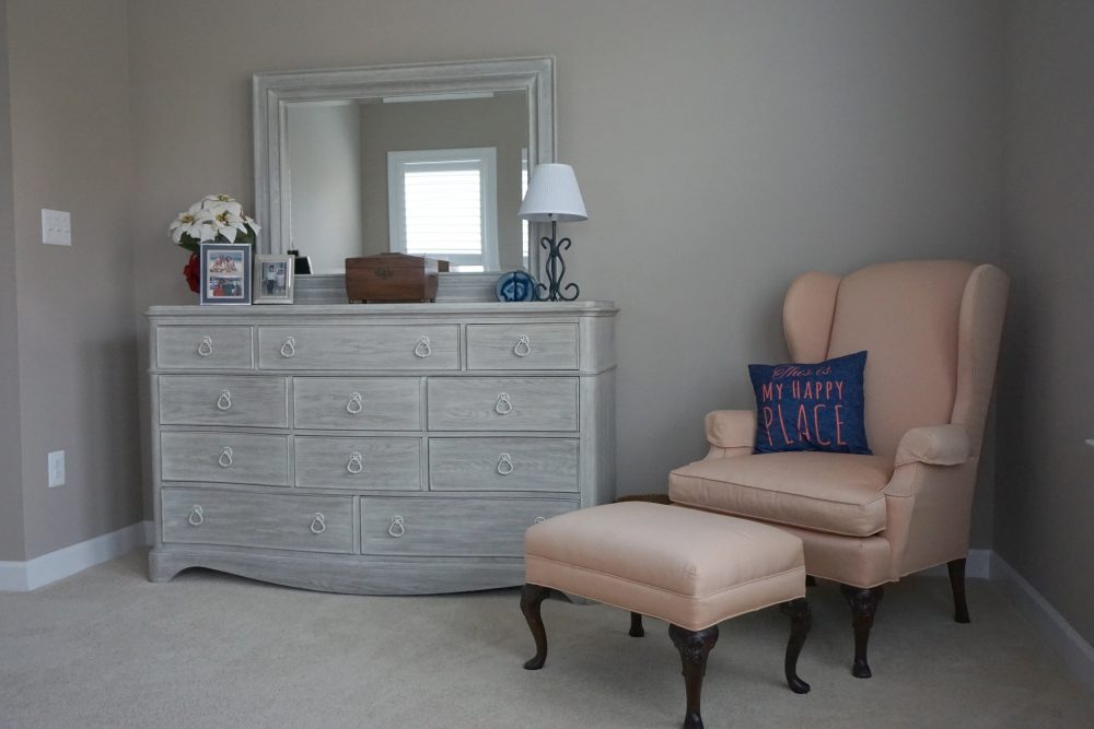 a bedroom with a dresser, chair and mirror